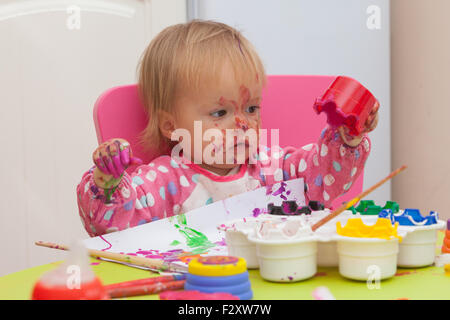 Ein 16 Monate alt, Blond Haare, Bürsten kaukasisch, Mädchen spielen mit Farben und die Farbe während des Sitzens im Inneren an einem kleinen Tisch. Stockfoto