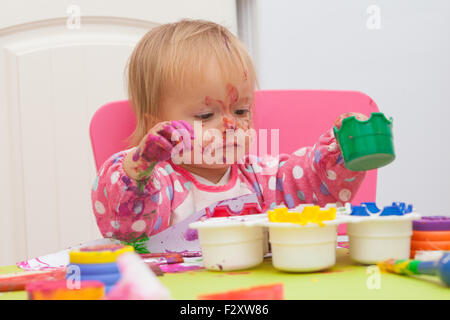 Ein 16 Monate alt, Blond Haare, Bürsten kaukasisch, Mädchen spielen mit Farben und die Farbe während des Sitzens im Inneren an einem kleinen Tisch. Stockfoto
