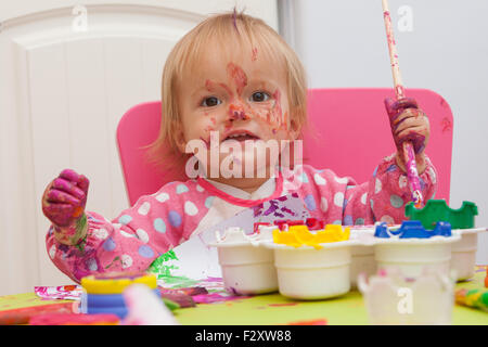 Ein 16 Monate alt, Blond Haare, Bürsten kaukasisch, Mädchen spielen mit Farben und die Farbe während des Sitzens im Inneren an einem kleinen Tisch. Stockfoto