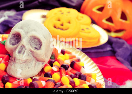 Nahaufnahme einer Platte mit Halloween Süßigkeiten und ein Schädel und einige Kürbis-förmigen Cookies mit beängstigend Ornamenten im Hintergrund, s Stockfoto