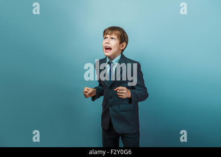 ein Junge von zwölf europäischen aussehen in einem Anzug schreien wütend auf grauem Hintergrund Stockfoto