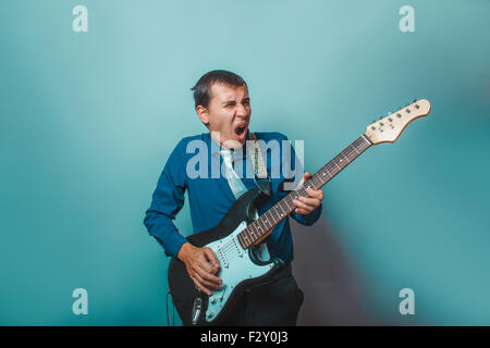 ein Mann der Europäischen Erscheinungsbild dreißig Jahren Gitarre zu spielen, auf einem grauen Hintergrund Stockfoto