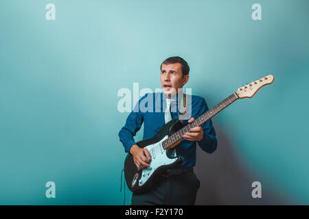 ein Mann der Europäischen Erscheinungsbild dreißig Jahren Gitarre zu spielen, auf einem grauen Hintergrund Stockfoto