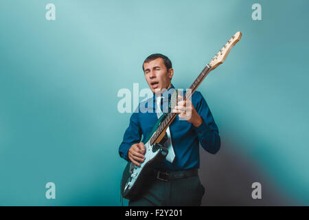 ein Mann der Europäischen Erscheinungsbild dreißig Jahren Gitarre zu spielen, auf einem grauen Hintergrund Stockfoto