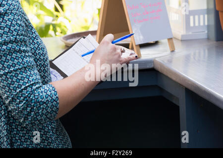 Eine Person in einem Café hält eine Rechnung und einen Stift Stand durch einen Balken zu begegnen, eine Speisekarte an Bord auf dem Display. Stockfoto