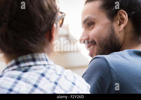 Ein junger Mann und eine Frau sitzen nebeneinander, lächelnd und reden. Stockfoto