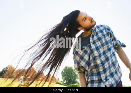 Ein junger Mann im Stich sein sehr langes dunklen Haares und schüttelte den Kopf, um es draußen an der frischen Luft Ventilator. Stockfoto