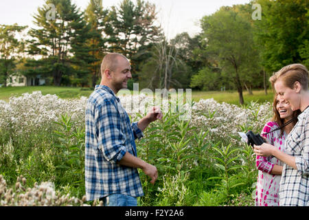 Drei Menschen, ein Mann und zwei Frauen in einer Wildblumenwiese stehen. Eine Frau hält eine Kamera mit Birne Flash-Anlage. Stockfoto