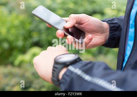 Mann mit Handy laufen an eine Smartwatch angeschlossen. Close-up Hände Stockfoto