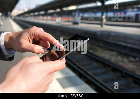 Mann mit Hilfe eines Mobiltelefons auf leeren Bahnsteig. Close-up Hände Stockfoto