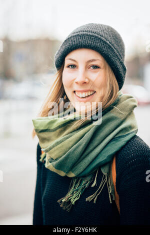 Porträt des jungen schönen Hipster sportliche blonde Frau, in der Kamera suchen, lächelnd - tragen einen Schal, eine Mütze und einen schwarzen Pullover - Glück, Jugend, Sorglosigkeit Konzept Stockfoto