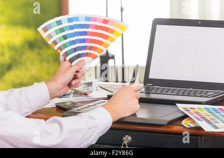 Männliche Hände hochhalten Palette, Colormap ausgebreitet vor Laptop am Schreibtisch Stockfoto