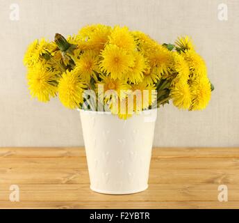 Bouquet von Löwenzahn in kleinen weißen Eimer auf leichten braunen Holztisch Stockfoto