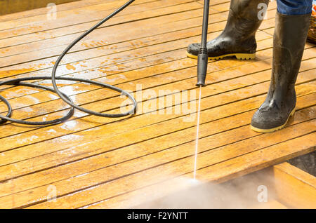 Mann trägt Gummistiefel mit hohem Wasserdruck Reiniger auf Holzterrasse Oberfläche. Stockfoto