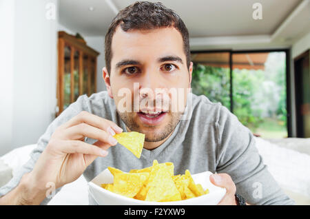 Closeup hispanische männlichen tragen helle blauen Pullover hält Schüssel mit Kartoffel-Chips vor Kamera, lustige Winkel Stockfoto