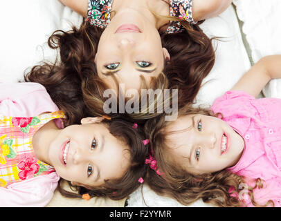 Junge liebenswerte hispanische Schwestern mit Mutter liegend, Köpfe berühren und Körper verteilt verschiedene Richtungen closeup Stockfoto