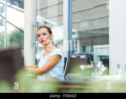 Attraktive junge Frau mit roten Lippen liest eine Zeitung, die sitzen in einem café Stockfoto