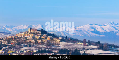 Kleinstadt auf dem verschneiten Hügel und Berg Grat auf Hintergrund im Piemont, Norditalien. Stockfoto