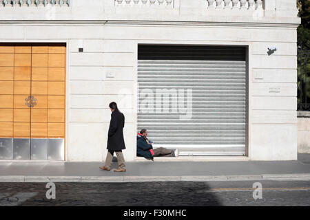 Obdachlos in Rom. Ein Obdachloser sitzt in einer Ladentür und zieht die Aufmerksamkeit eines Passanten auf sich. Via Nazionale, Rom, Italien. Stockfoto