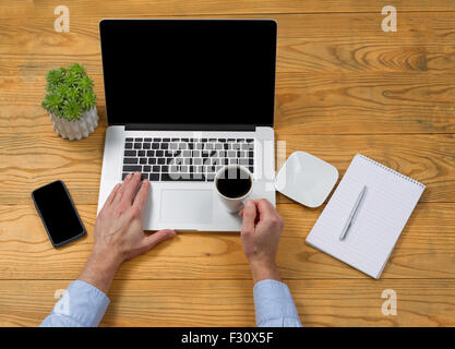 Hoher seitlicher Blick auf männliche Hand, die Tasse Kaffee beim Tippen auf der Computertastatur. Stockfoto