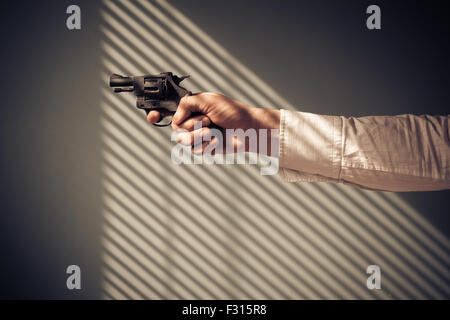 Mann zeigt einen Revolver an einem Fenster mit Schatten von den blinds Stockfoto