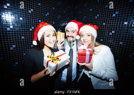 Fröhliche Unternehmensgruppe in festlich gekleidet und Santa Caps zeigen ihre Geschenke Stockfoto