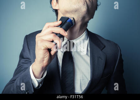Ein junger Geschäftsmann ist mit einen elektrischen Rasierapparat Rasieren. Stockfoto