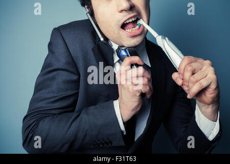 Gestressten Geschäftsmann ist am Telefon beim Zähneputzen und rasieren um Zeit zu sparen Stockfoto