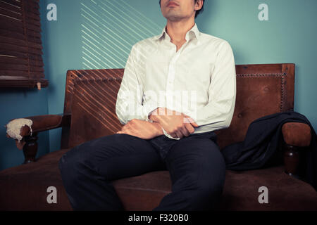 Junger Mann ist an einem sonnigen Tag entspannen Sie sich auf ein altes Sofa am Fenster Stockfoto