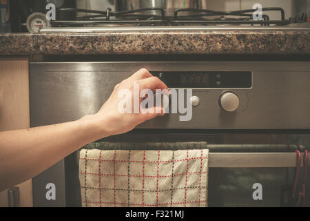 Die Hand einer jungen Frau dreht den Knopf auf dem Herd Stockfoto