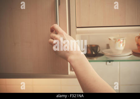 Die Hand einer jungen Frau ist ein Küchenschrank öffnen. Stockfoto