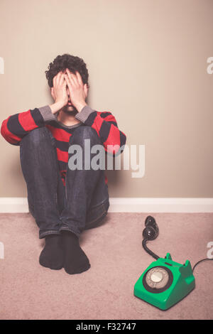 Müde und trauriger junger Mann sitzt auf dem Boden mit einem Telefon Stockfoto