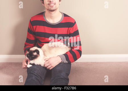 Ein junger Mann sitzt auf dem Boden und seine Katze streicheln Stockfoto