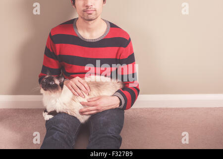 Ein junger Mann sitzt auf dem Boden und seine Katze streicheln Stockfoto