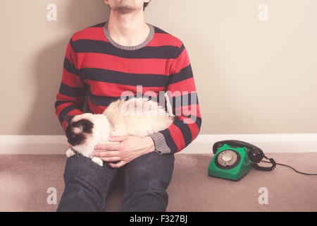 Junger Mann sitzt auf dem Boden mit seiner Katze und Telefon Stockfoto