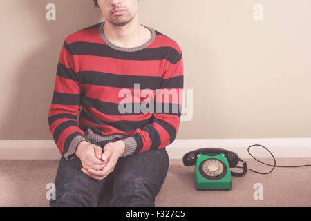 Junger Mann sitzt auf dem Boden mit einem alten rotary Telefon Stockfoto