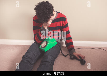 Trauriger Mann auf dem Boden sitzend hat schlechte Nachrichten am Telefon erhalten. Stockfoto