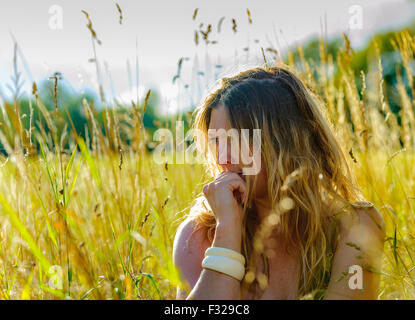 Eine Hintergrundbeleuchtung Porträt einer Frau (im Alter von 25-30) saß in einem Feld lange Gras an einem Sommerabend Stockfoto