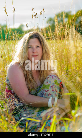 Eine Hintergrundbeleuchtung Porträt einer Frau (im Alter von 25-30) saß in einem Feld lange Gras an einem Sommerabend Stockfoto