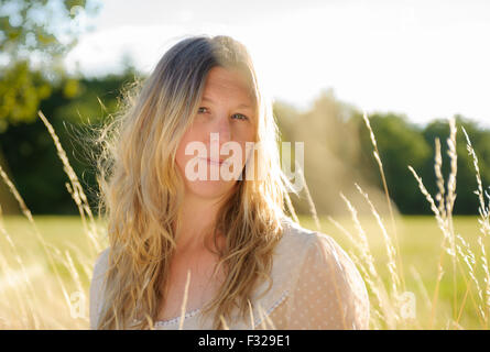 Eine Hintergrundbeleuchtung Porträt einer Frau (im Alter von 25-30) trägt ein weißes Top, saß in einem Feld lange Gras an einem Sommerabend Stockfoto