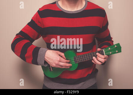 Junger Mann in einem gestreiften Pullover spielt ukulele Stockfoto