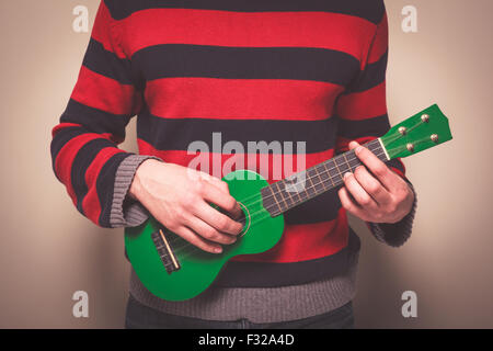 Junger Mann in einem gestreiften Pullover spielt ukulele Stockfoto