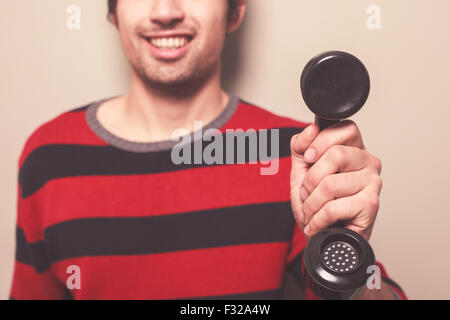 Ein glücklicher junger Mann hält einen Telefonhörer Stockfoto