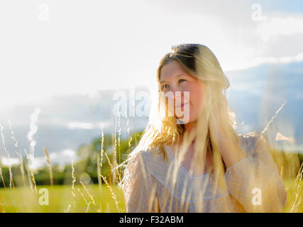 Eine Hintergrundbeleuchtung Porträt einer Frau (im Alter von 25-30) trägt ein weißes Top, saß in einem Feld lange Gras an einem Sommerabend Stockfoto