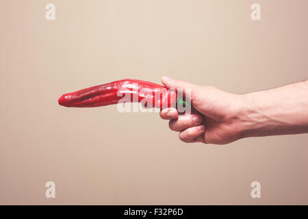 Die Hand eines Mannes ist eine roter Pfeffer wie eine Waffe halten. Stockfoto