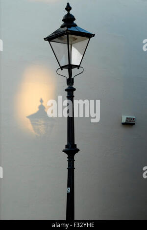 eine altmodische Straßenlaterne wirft einen Schatten an der Wand wie Sonnenlicht durch sie reflektiert wird Stockfoto