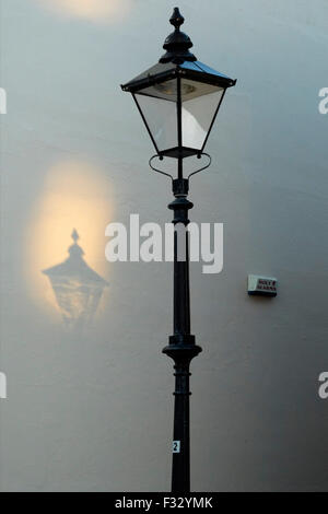 eine altmodische Straßenlaterne wirft einen Schatten an der Wand wie Sonnenlicht durch sie reflektiert wird Stockfoto