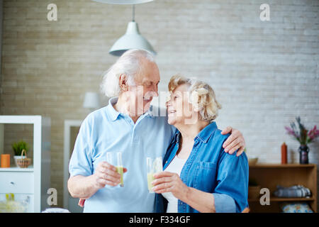 Ältere Mann und Frau halten Gläser mit gesunde hausgemachte Fruchtsaftgetränk und schauen einander an Stockfoto