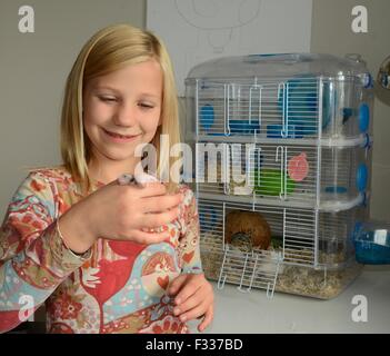 Schwedische Blondine, neun Jahre alt, hält Neugeborene Hamster, vor einem Hamsterkäfig, Ystad, Schweden Stockfoto