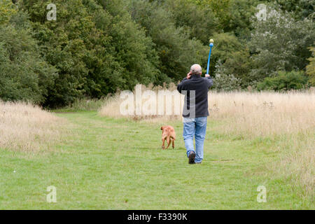 Mann, telefonieren mit Handy während Ballweitwurf mit Chuck-It Spielzeug für Hund in Landschaft in Bedford, Bedfordshire, England Stockfoto